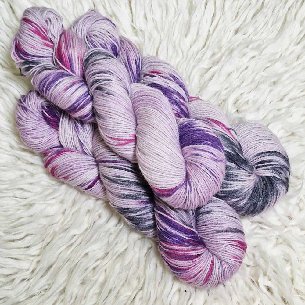 Drei Stränge handgefärbte Sockenwolle in Violett- und Rosa-Tönen auf weißem Fell Hintergrund.