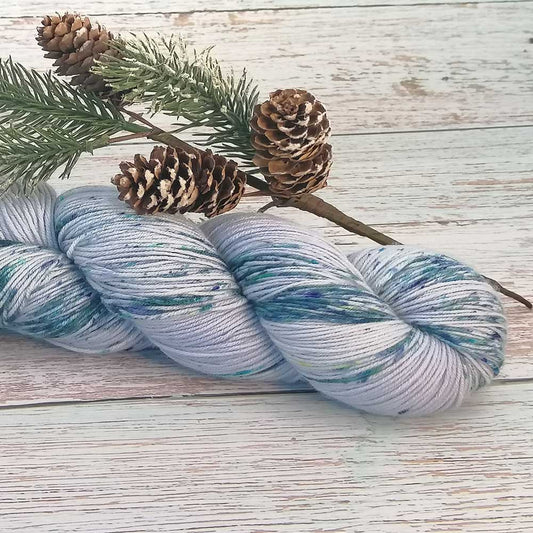 Handgefertigtes Desiree Garn in sanften Blau- und Grautönen mit feinem Glitzereffekt auf hellem Holzuntergrund.