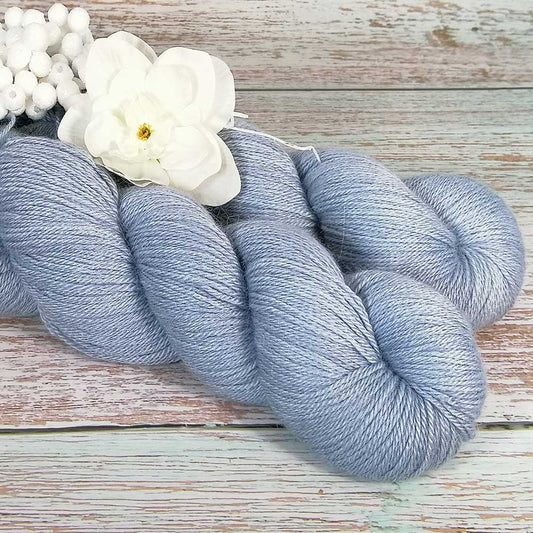 Handgefertigtes Strickgarn in zartem Aqua-Blau, weich und glänzend, auf rustikalem Holzhintergrund mit weißen Blüten.
