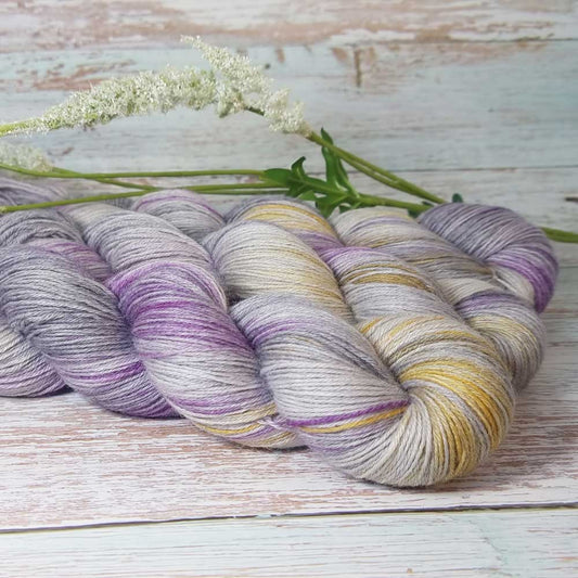 Lila und grauer Bambus-Strickgarn mit gelben Akzenten, locker zusammengedreht auf Holzbrett.