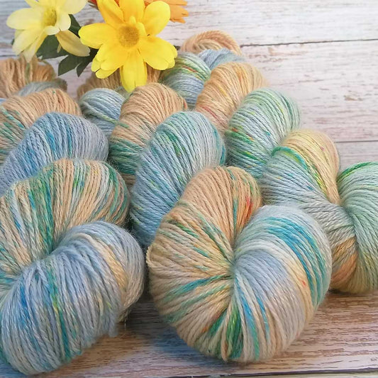 Handgefertigte Merino Tencel Wolle in Pastellfarben Blau, Grün und Beige, locker auf Holztisch arrangiert mit gelben Blumen.