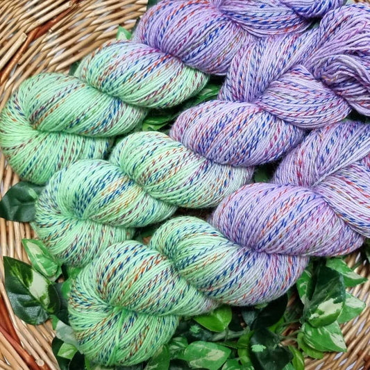 Mehrfarbige Stricksockenwolle in Pastelltönen Lavendel und Apfelgrün, gedreht und in einem Korb angeordnet.