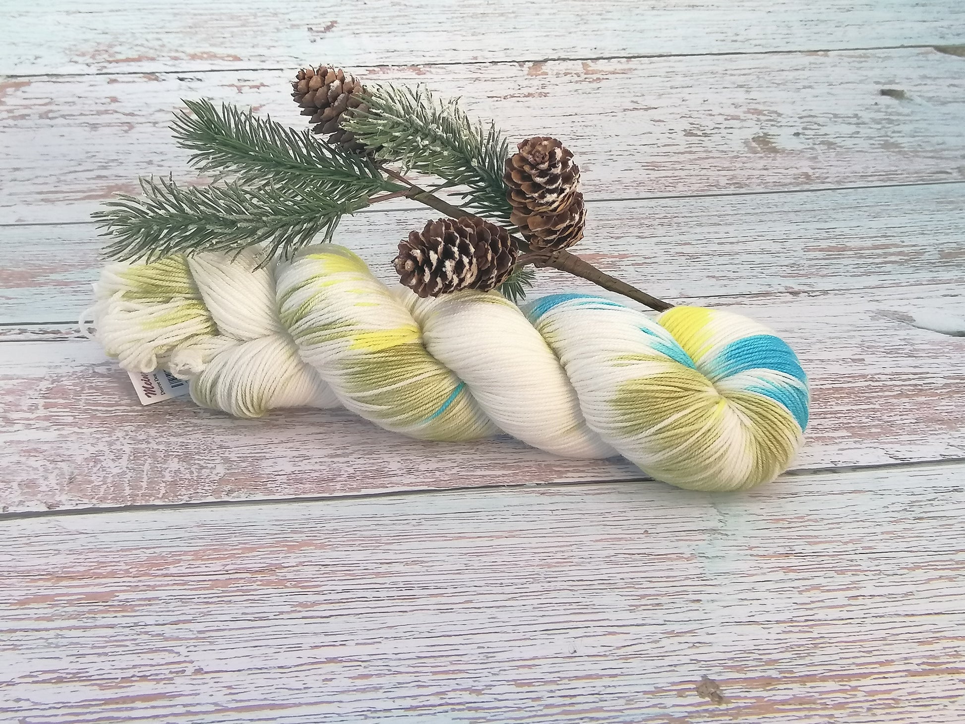 Handgefertigtes Garn in Weiß mit Farbakzenten in Gelb und Hellblau, locker gedreht, liegend auf Holzbrett.