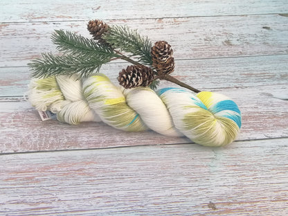 Handgefertigtes Garn in Weiß mit Farbakzenten in Gelb und Hellblau, locker gedreht, liegend auf Holzbrett.