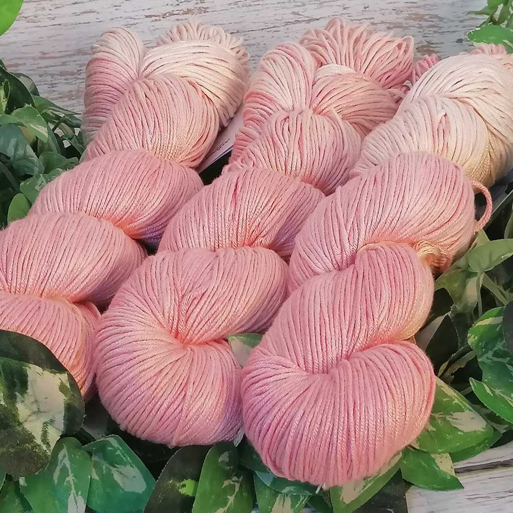 Handgefertigte weich glänzende Rosé-farbene Wollknäuel in Rosé- und Rosenquarz-Tönen, arrangiert auf grünem Blattwerk.