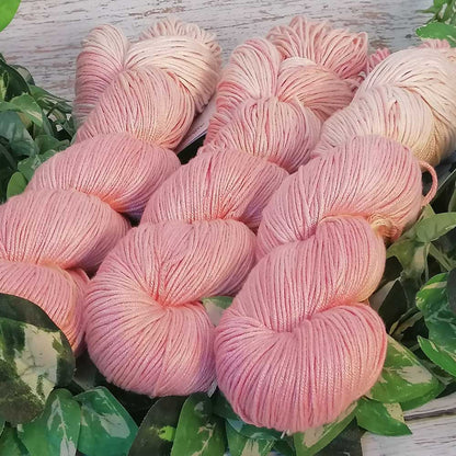 Handgefertigte weich glänzende Rosé-farbene Wollknäuel in Rosé- und Rosenquarz-Tönen, arrangiert auf grünem Blattwerk.