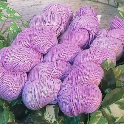 Handgefertigte Arcadia Garnstränge in sanftem Lilac, locker aufgewickelt und auf grünen Blättern arrangiert.