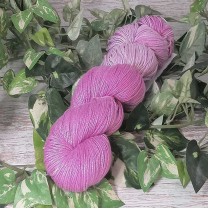 Handgefertigtes Strickgarn in leuchtendem Lilac mit feiner Textur, auf grünem Efeuarrangement liegend.