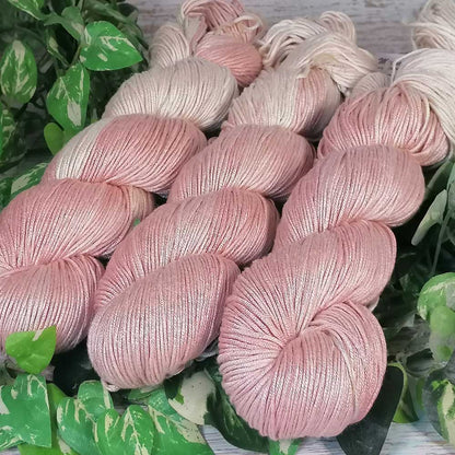 Handgefertigte, zarte Arcadia-Garnstränge in pastellrosa Rosenquarzfarben, liegend auf grünen Blättern.