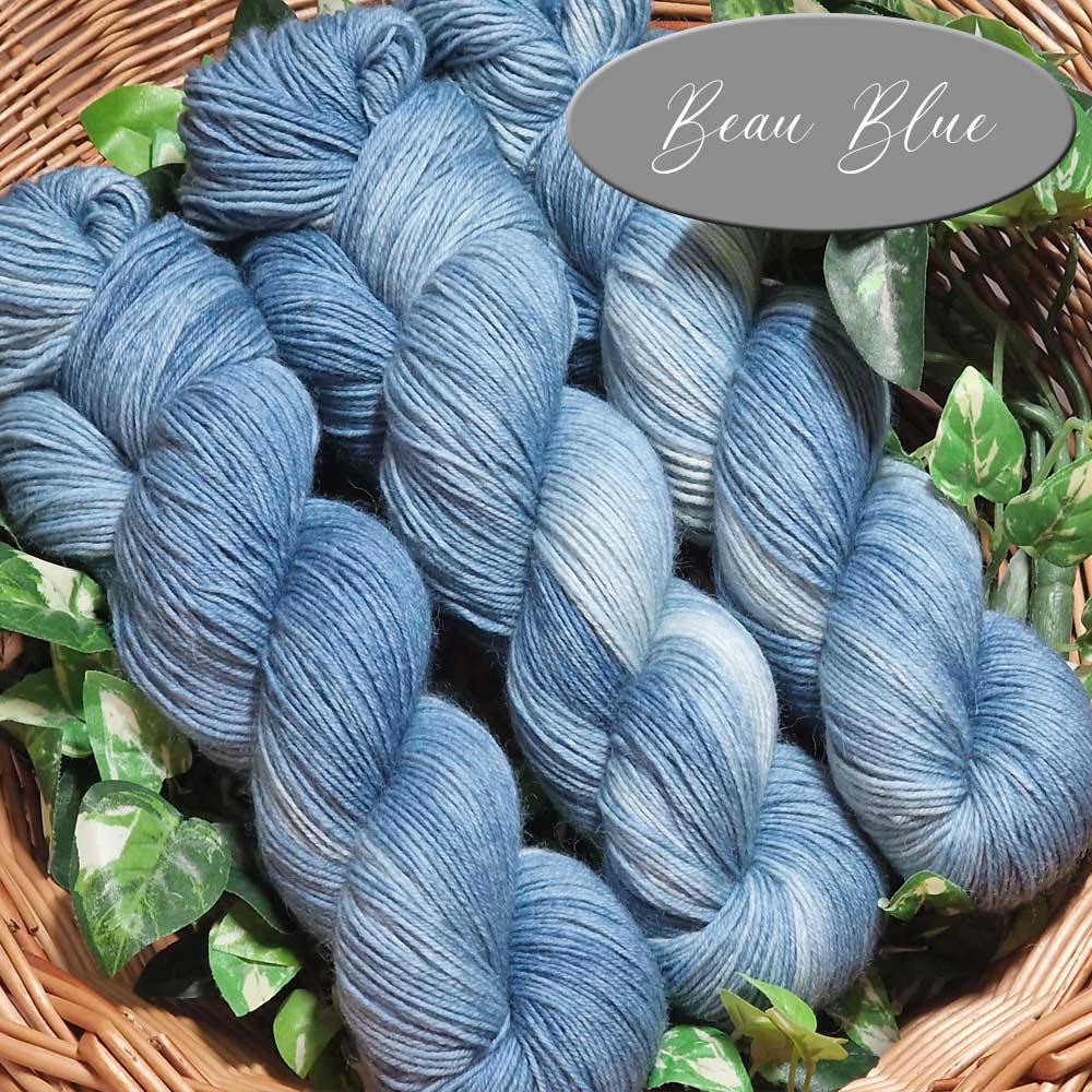 Mehrere Stränge weicher, blau-grauer Sockengarne in Naturkorb mit grünen Blättern.