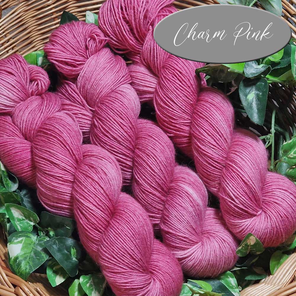 Weiche Strickwolle in leuchtendem Pink, farblich als Charm Pink gekennzeichnet, in lockerer Strangform angeordnet.