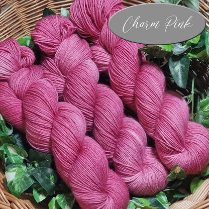 Weiche Strickwolle in leuchtendem Pink, farblich als Charm Pink gekennzeichnet, in lockerer Strangform angeordnet.