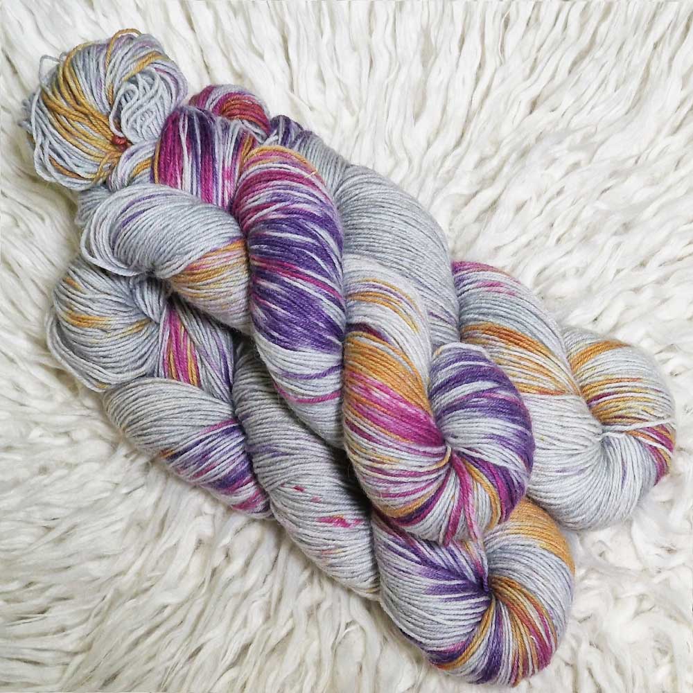 Drei Stränge mehrfarbiger Sockengarn in Grau, Lila, Gelb und Rot auf weißem Hintergrund.