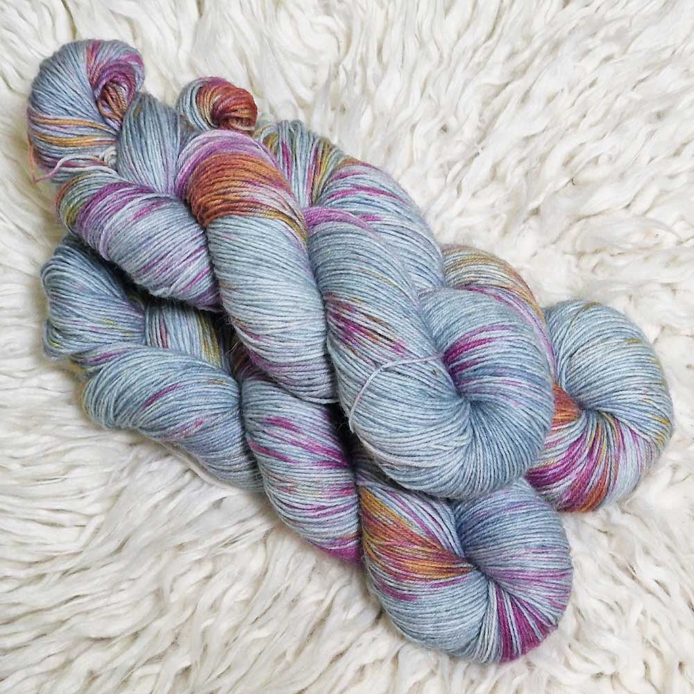 Garnstränge in hellblau mit violetten und orangen Sprenkeln auf weißem Fellhintergrund.