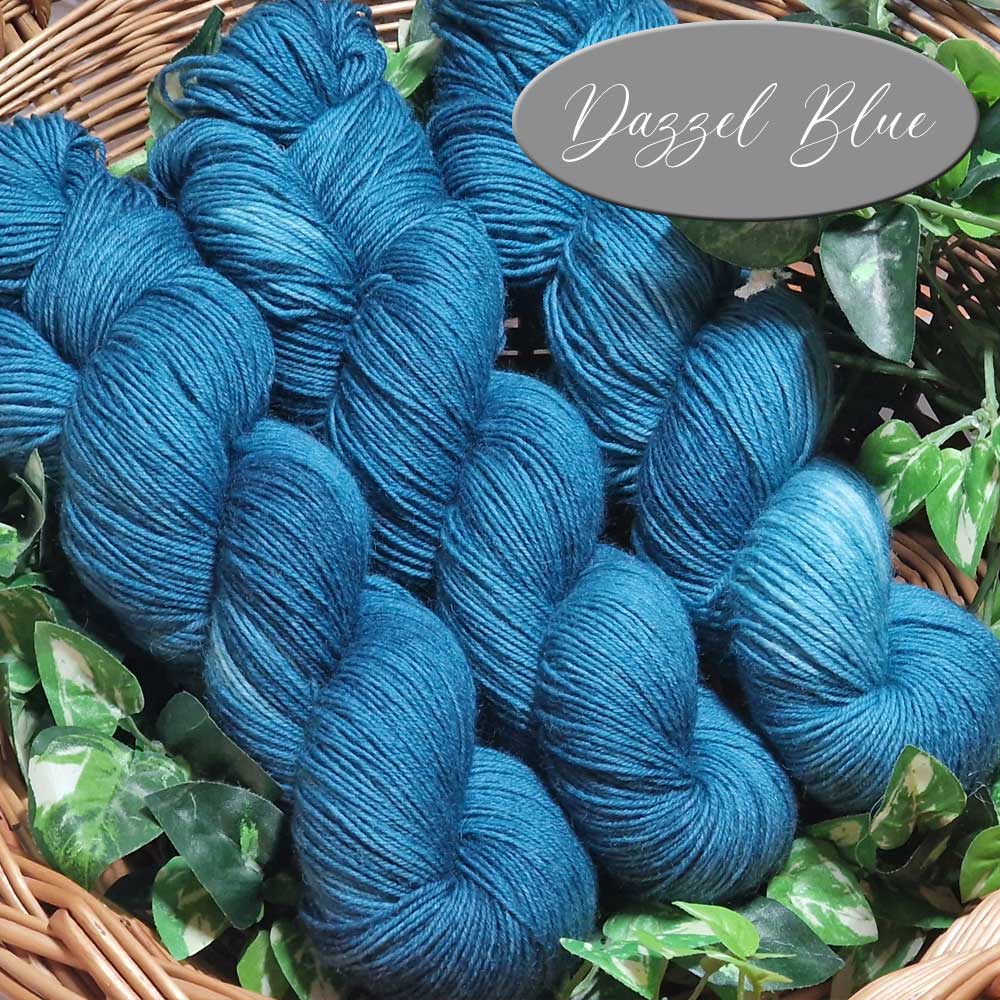 Stränge von feiner, glänzender Wolle in lebendigem Dazzel Blue, arragiert in einem Korb mit grünen Blättern.