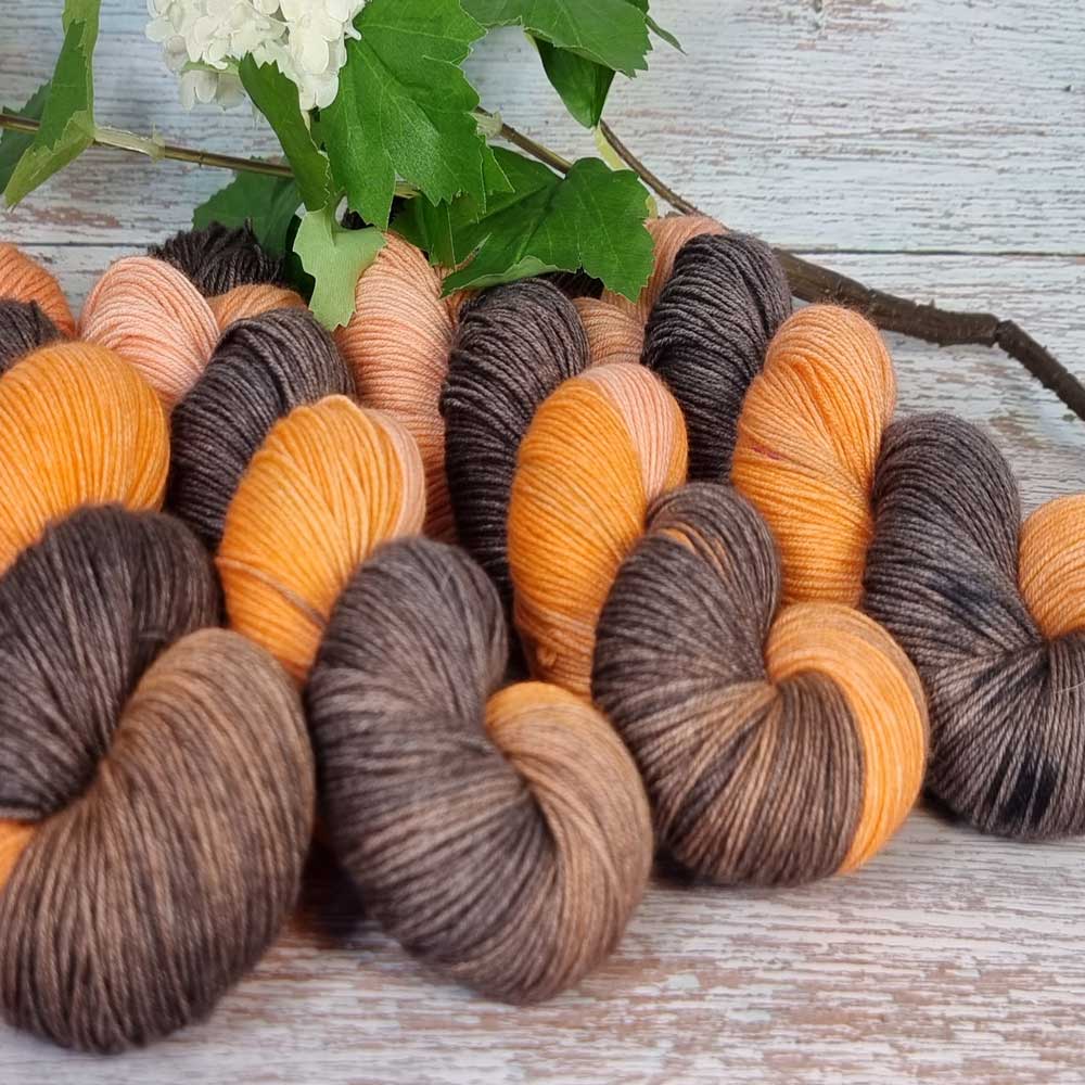 Handgefertigte Desiree Garnstränge in warmen Orange- und Braun­tönen, locker gedreht auf rustikalem Holzhintergrund mit.
